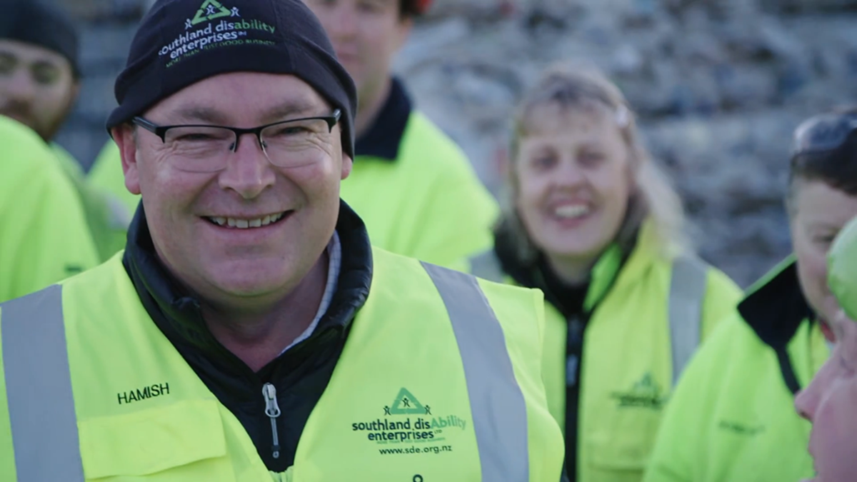 Hamish McMurdo outside with his employees wearing a yellow vest.