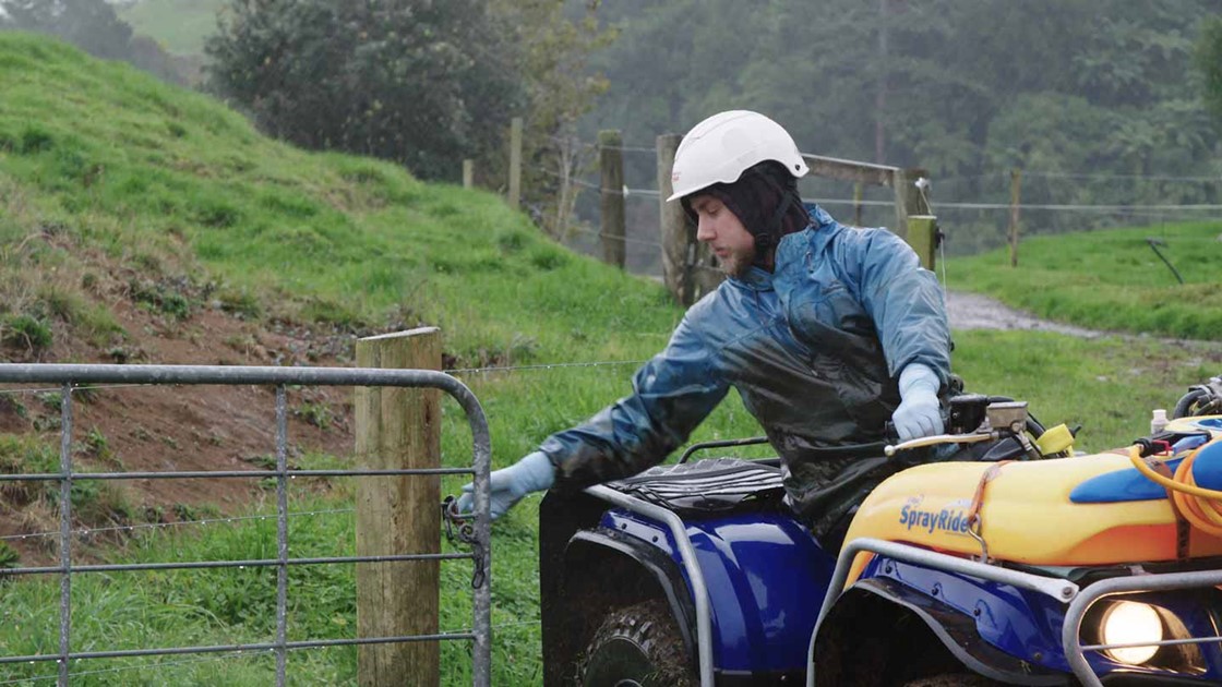 Jack on a quadbike closing a paddock gate dressed in wet-weather gear.