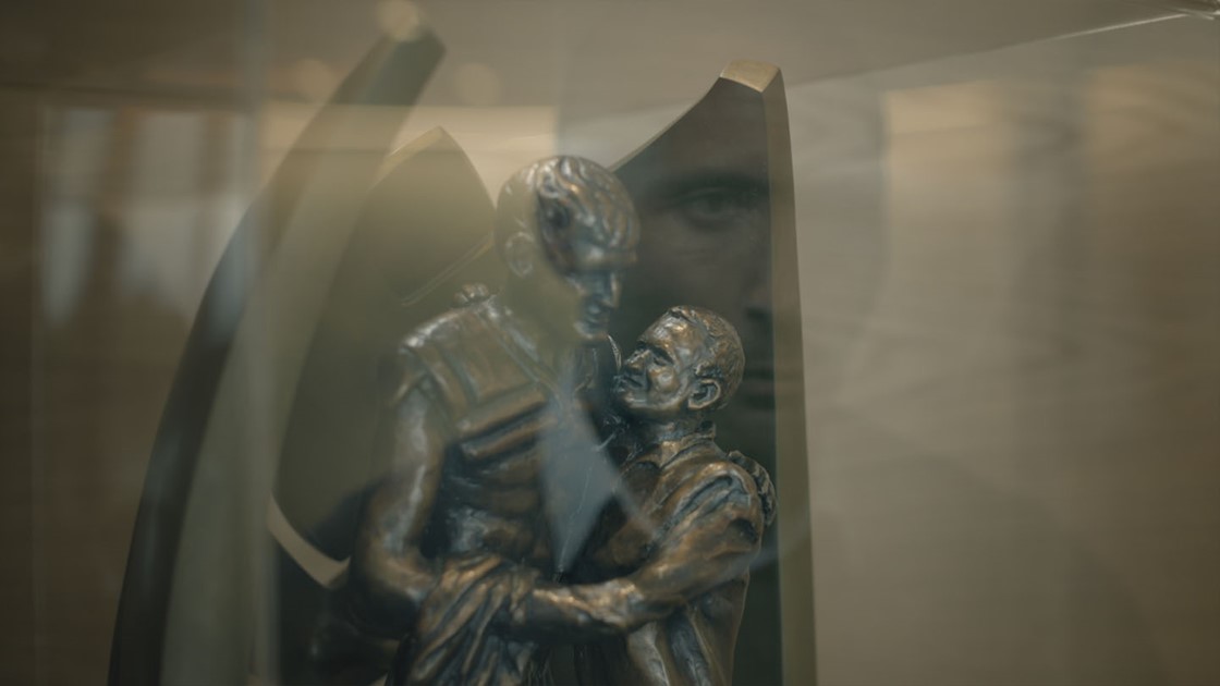 Paul's reflection overlaying a metal statue of a man and a boy hugging. 